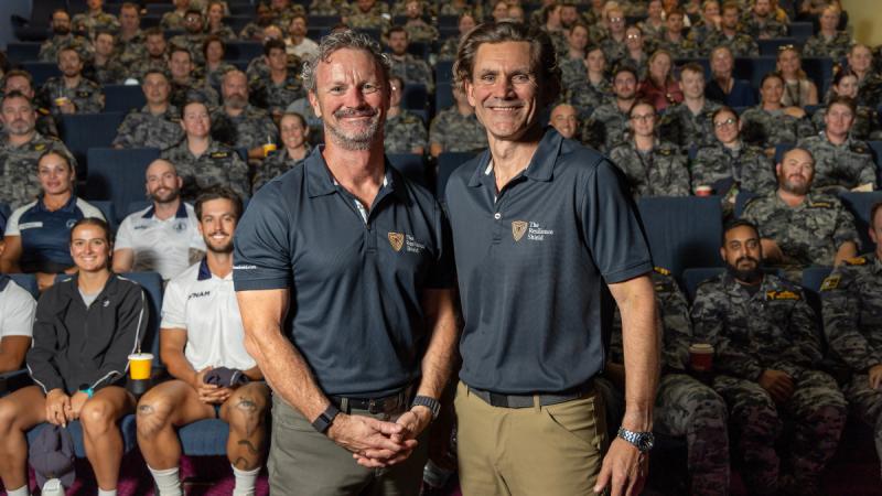 Two men stand before a crowded theatre.