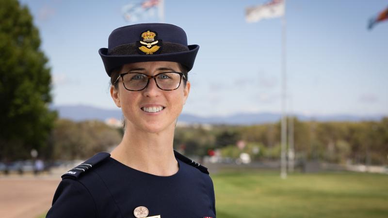 A military woman stands outside in front of several raised flags.