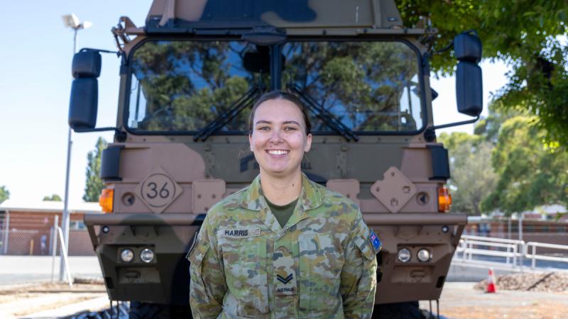 A woman in Army uniform standing in front of a medium truck.