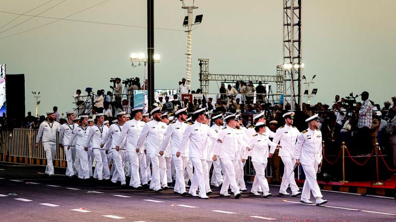 Uniformed Navy personnel march in formation along a road,