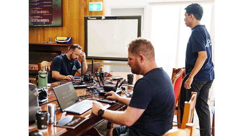 Three men work inside on laptops.
