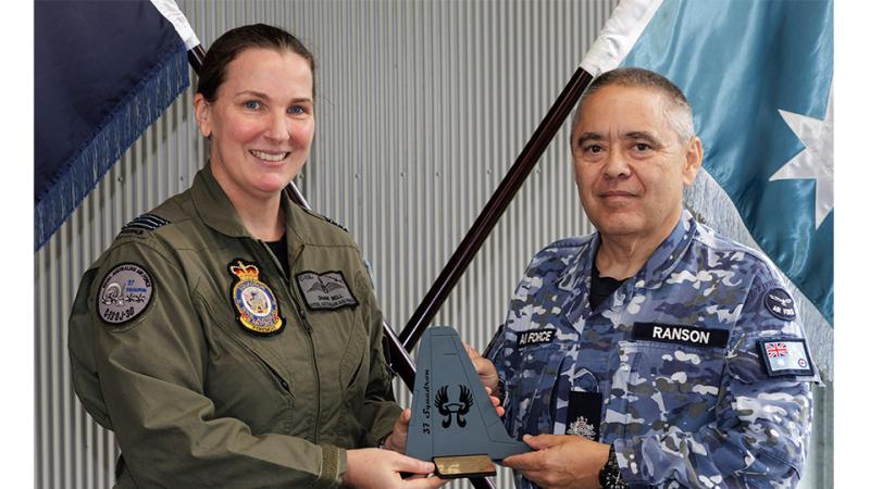 A woman in military uniform presents an award shaped like a Hercules aircraft tail to a man in military uniform.