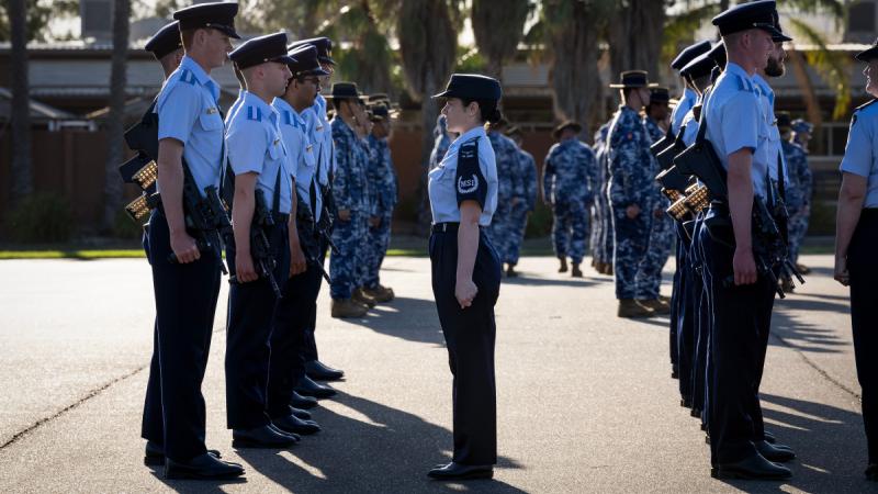 A uniformed woman stands between rows of uniformed people holding rifles, facing the back row.