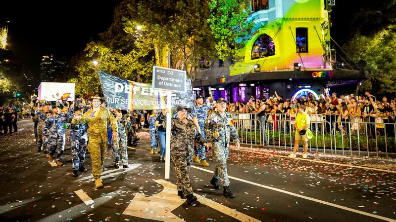Defence personnel march in a group past a colourful building on a Sydney street.