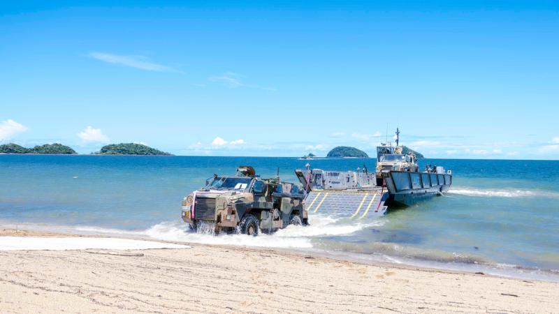 An Army vehicle drives from a boat onto the shore of a beach.