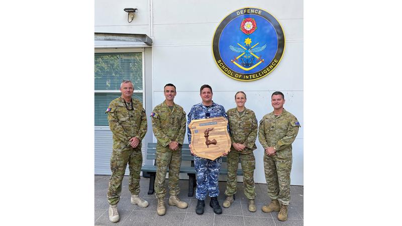 Five military men stand with an award outside a building.