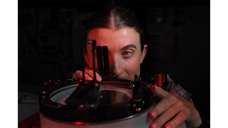 A military woman looks through the lens of a device.