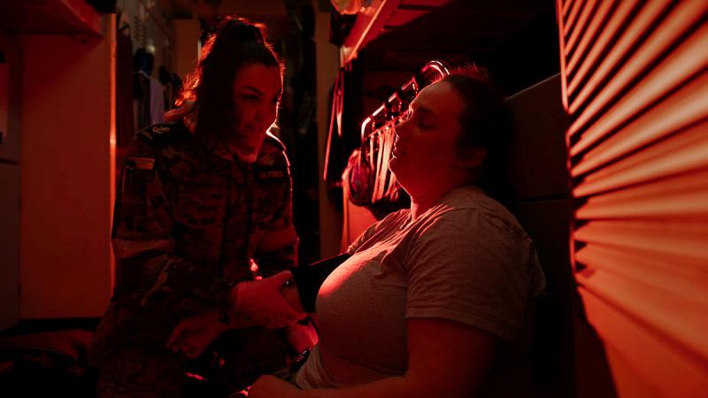 A Navy member tends to a mock casualty in a red-lit room.