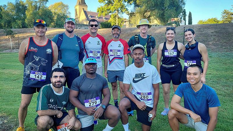 ADF personnel in running gear stand and kneel in a grassy area. 