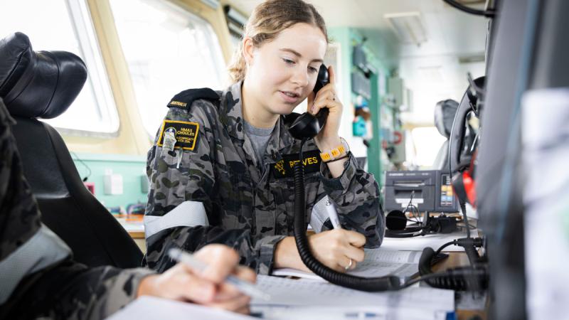 HMAS Choules sailor, Seaman Communications Information Systems Laura Reeves holds a phone up to her ear as she conducts a COMEX (communications training) with partner nations during Exercise KAKADU 26.