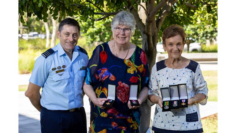A military man and two women holding five medals between them.