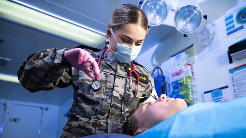 A Navy medic in uniform works on a fake patient.