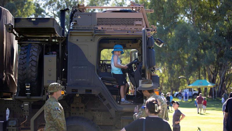 An Army member watches a child inside an Army truck with other people looking on.