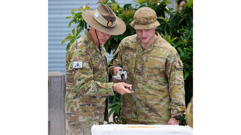 Two men in Army camouflage cutting a cake with a sword.