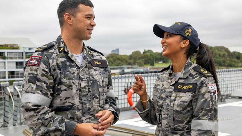 Two Navy personnel, a male and a female, talk on the flight deck of a ship.