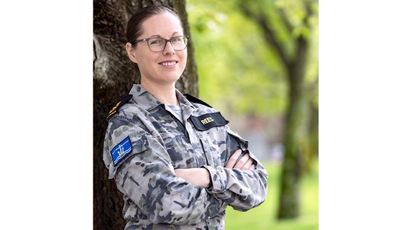 A military woman outside by a tree.