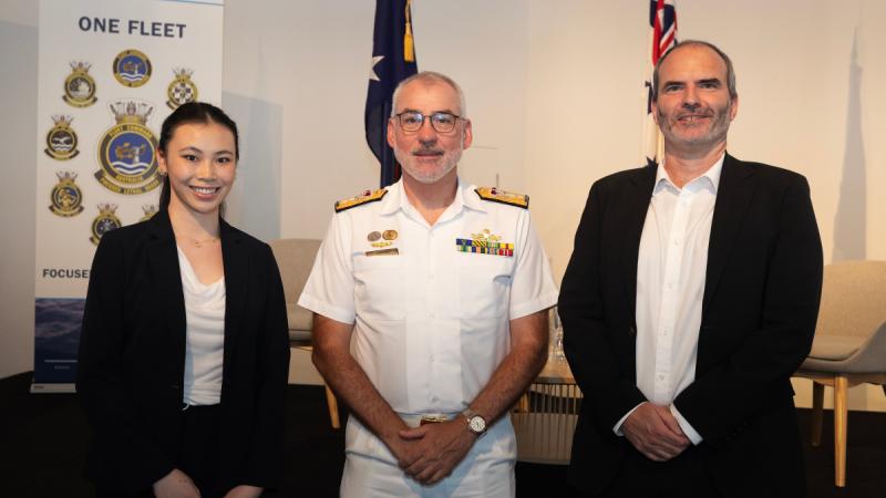Two university academics stand on either side of a Navy Rear Admiral.