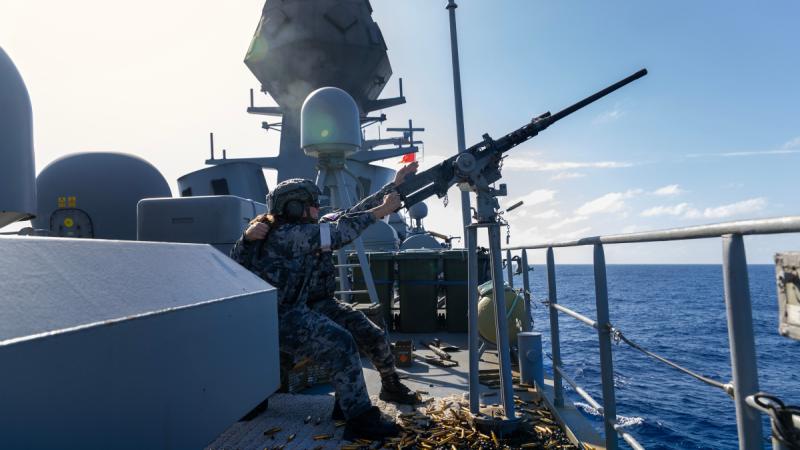 A military woman aims and shots a large weapon from a ship out at sea.