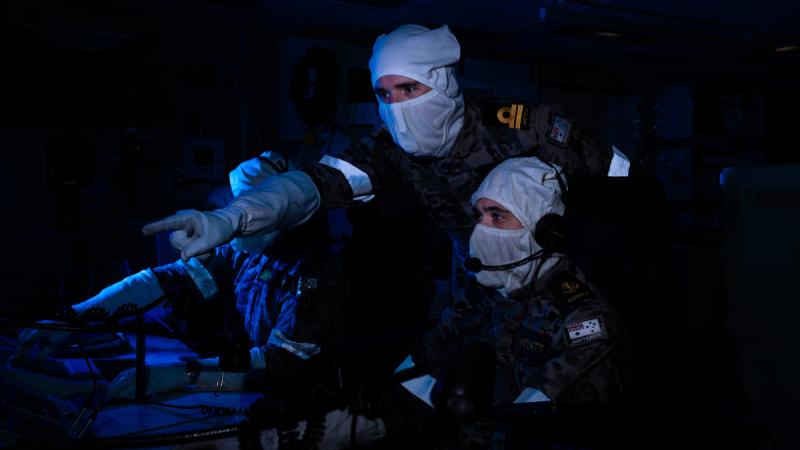 Two men in special uniform discuss something on a screen in the dark.