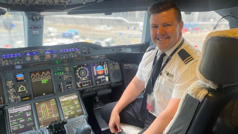 Man in cockpit of a Qantas A380 aircraft facing camera with control panel in the foreground.