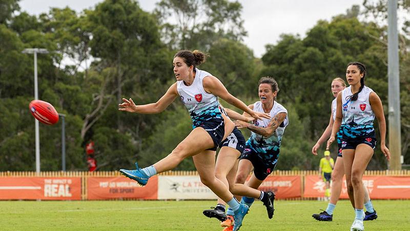 A woman kicks a football during an AFL game.