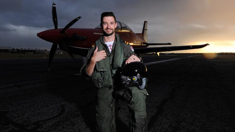 An aviator bends down on one knee in front of an aircraft.