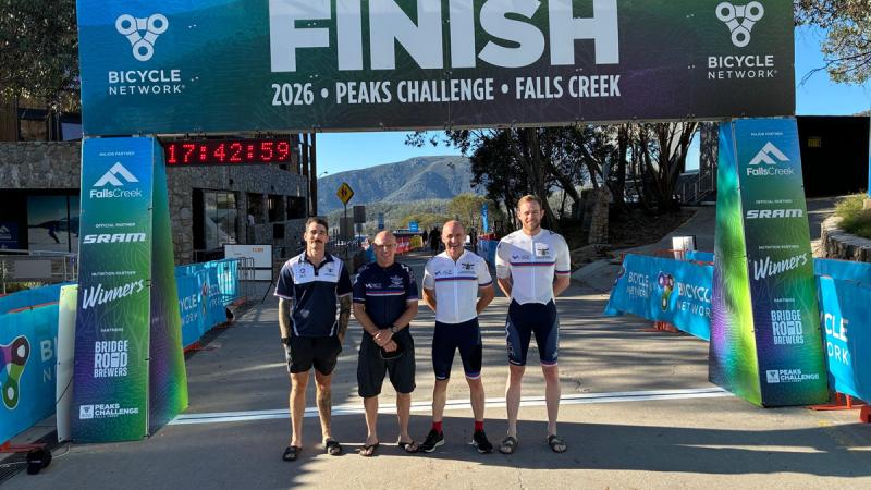 Four men in cycling gear standing in front of a finish sign.