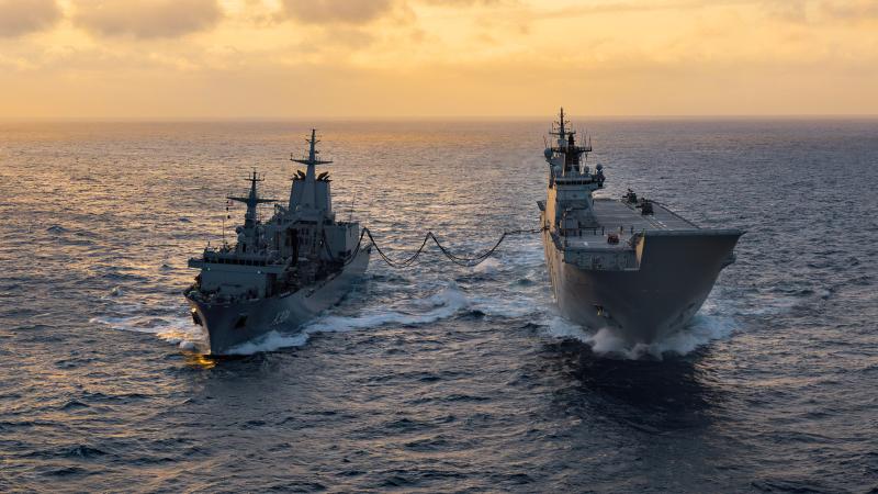 Two ships sailing side by side with a sunset in the background.