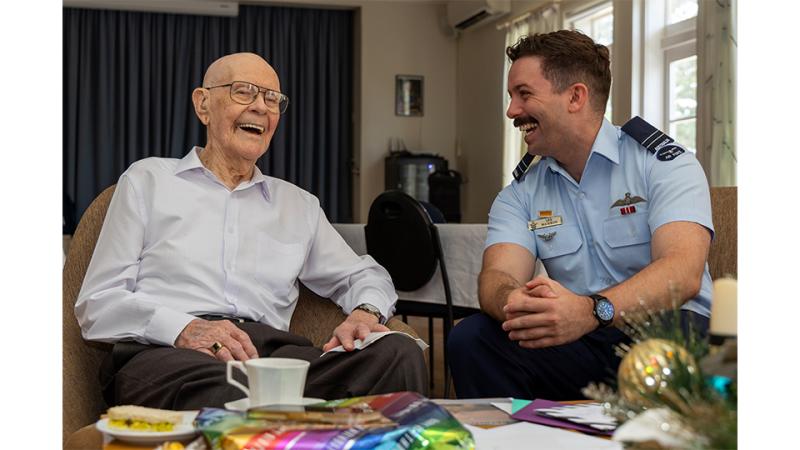 A military man and an elderly man laugh together.