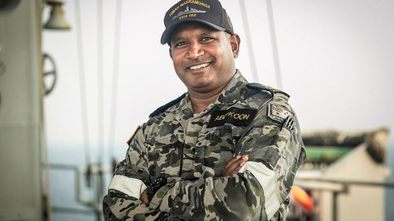 A sailor poses for a photo with his arms crossed and smiles.