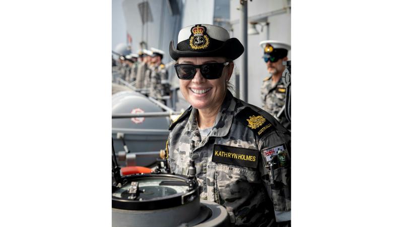 A Navy member sits in uniform facing the camera and smiling.