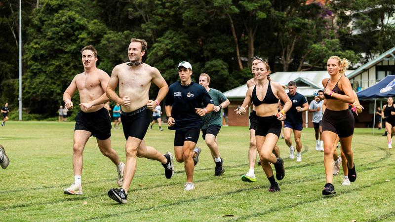 A group  people wearing exercise gear run on a grass track.
