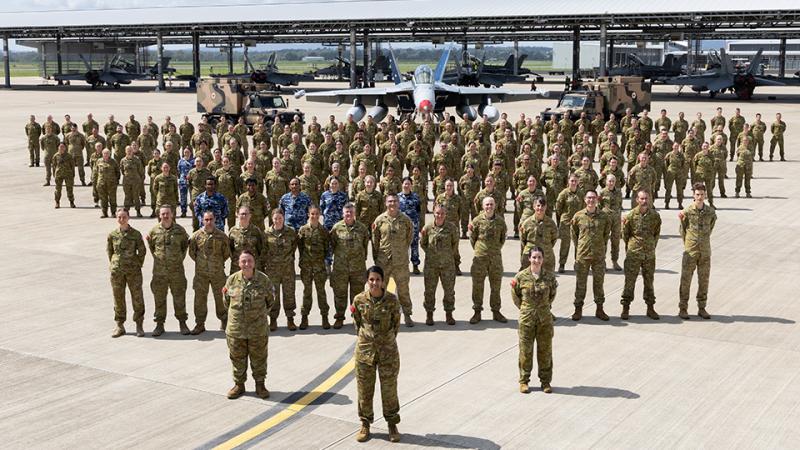 A large group of military personnel stand in a pyramid formation with their aircraft.