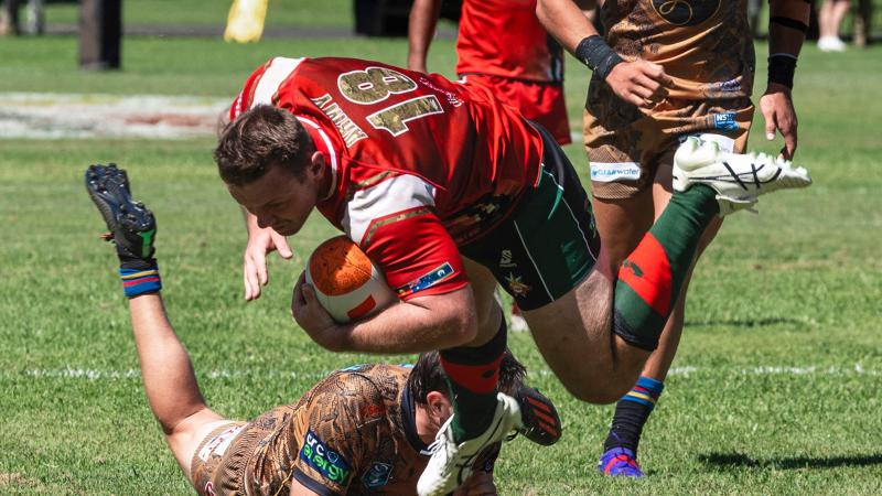 Army rugby player holds the football and pushes off an opponent.
