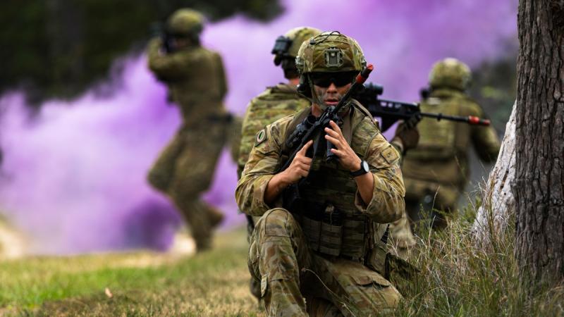 Army soldiers in a field holding guns with purple smoke in the background.