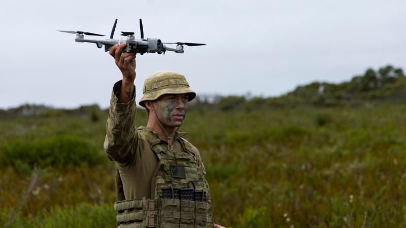 An Army soldier standing in a field holding a small drone.