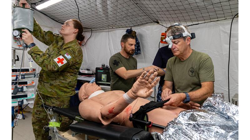Three military members perform medical procedures on a dummy. 