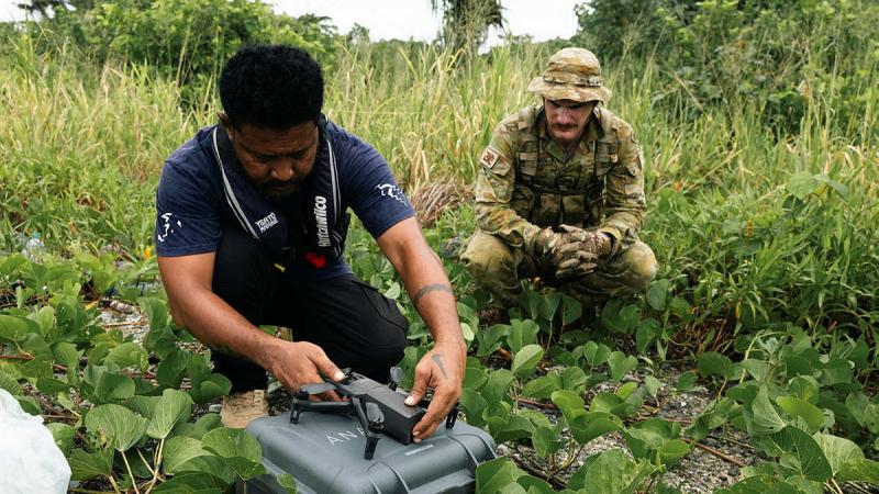A Solomon Islands man sets up a drone as an Australian Army member watches on.