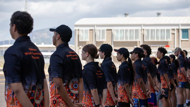 A large group of youth in matching uniform stand in a line outside.