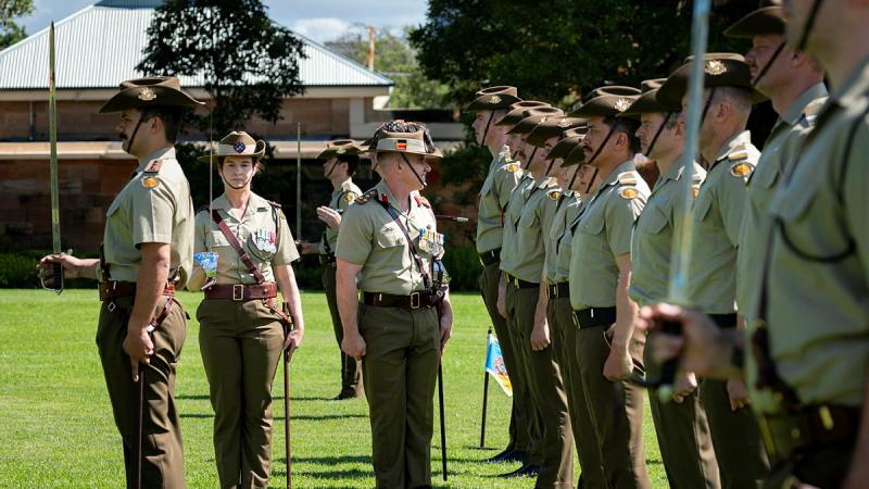 Army members walk by junior Army members, standing in line and at attention.
