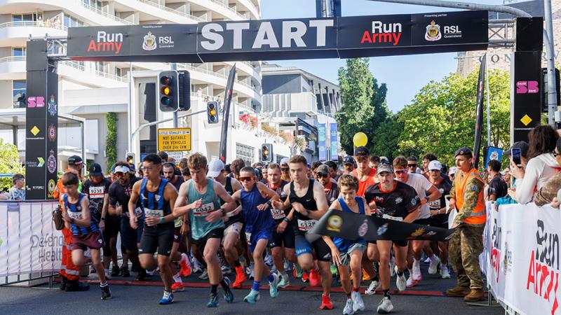 A dense group of runners passes beneath a Run Army start banner at the beginning of a race.
