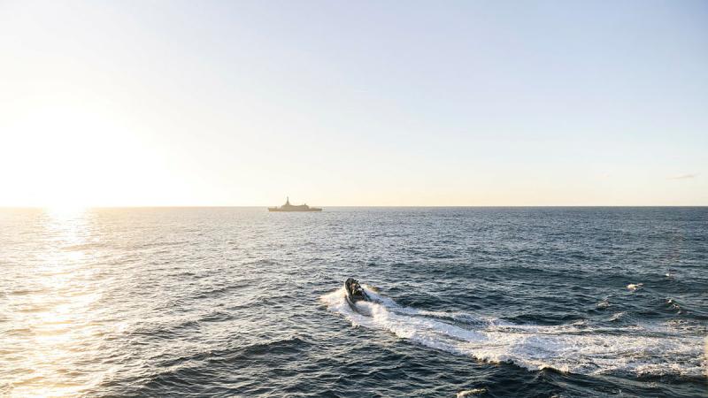 A small boat heads towards a ship on the horizon.