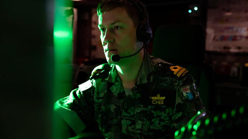 A sailor watches a screen in a dark room