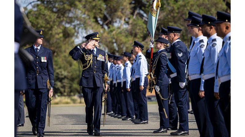 A military member salutes a line of personnel at attention.