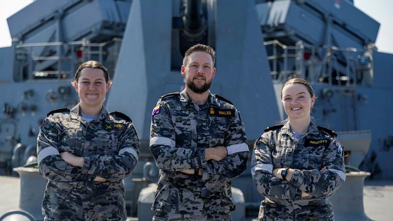 Three sailors stand on a ship with their arms crossed while at sea.