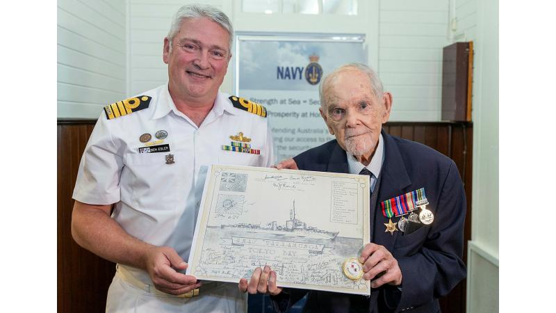 A Navy member presents a drawing of a ship to a veteran.