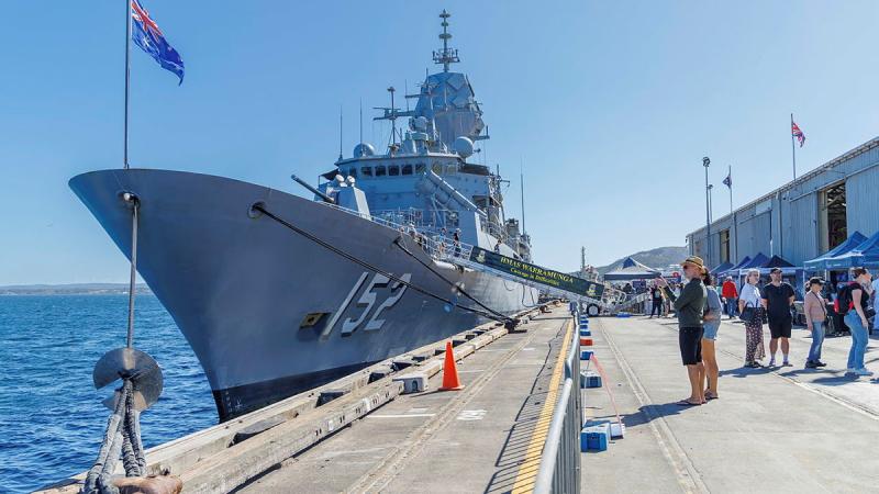 Locals look toward a Navy ship which is sitting next to a port.