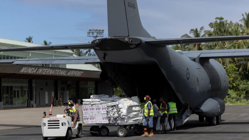 People in high-visibility vests transferring packages from the back of an aircraft onto a trailer on an airport tarmac.