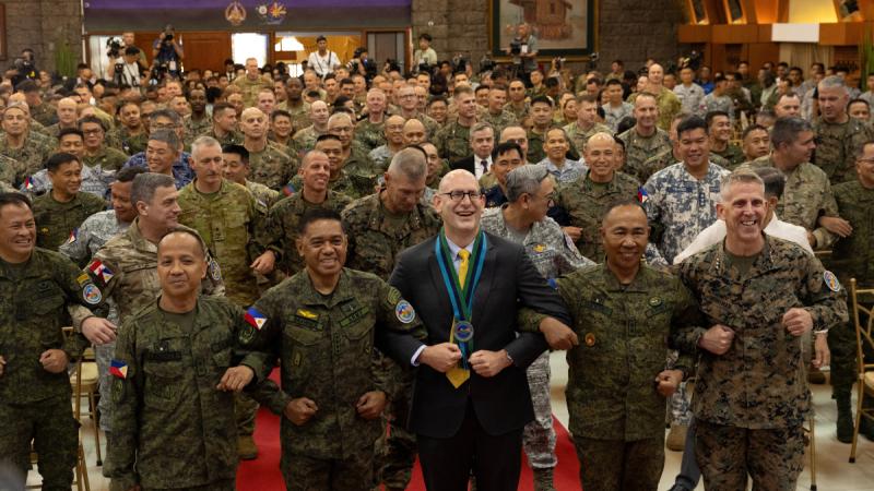 Rows of uniformed personnel stand closely together with their arms linked. 