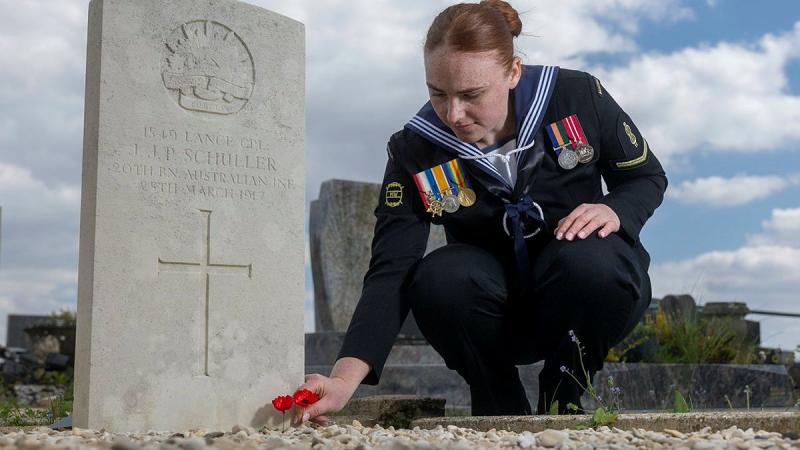A Navy member crouches to place a poppy on a grave.